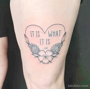 Фото тату сердца, обрамленного цветами, с надписью "IT IS WHAT IT IS" и инициалами "J.W". Эскиз татуировки выполнен в черно-белой гамме.