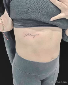 Фото тату: Минималистичная татуировка с надписью имени "Milagro", выполненная изящным шрифтом на боку.