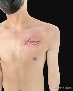 Фото тату на груди: надпись с именем "Leonor" и датами жизни "1937-2022", выполненная изящным шрифтом с добавлением символа креста.