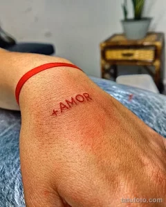 Фото минималистичного тату с надписью "AMOR" на запястье. Красный цвет и тонкие линии.