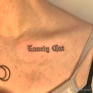 Фото готического тату с надписью "Lonely Cat" на груди. Черный шрифт в старинном стиле.