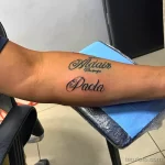 Фото каллиграфического тату с именами "Madair" и "Paola" на предплечье. Элегантный шрифт и дата.