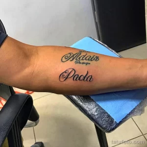 Фото каллиграфического тату с именами "Madair" и "Paola" на предплечье. Элегантный шрифт и дата.