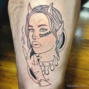 Фото тату на ноге: Изображение женского лица с рогами и надписью "Demon". Черно-белый рисунок татуировки в стиле графика.
