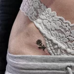 Фотография минималистичной татуировки с изображением маленькой черной розы на коже. Нежный и изящный рисунок татуировки.