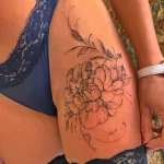 Фото тату: Один большой пион, выполненный в технике dotwork, с добавлением листьев и стеблей. Татуировка расположена на бедре.