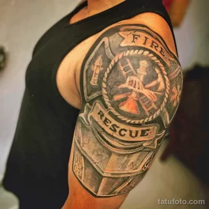 Фото тату: изображение пожарного знака с элементами шестеренок и надписями "Fire Rescue", выполненное в черно-серых тонах на плече.