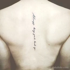 Фото тату: черная надпись 'Always keep your head up' вертикально вдоль позвоночника на спине мужчины. Минималистичный дизайн.