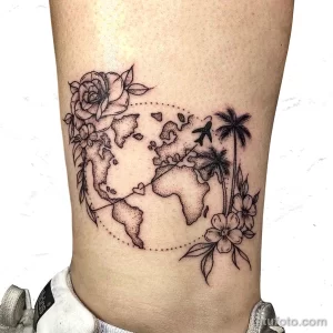 Фото тату на ноге с изображением глобуса, окруженного цветами, птицами и точками, символизирующими маршруты путешествий.