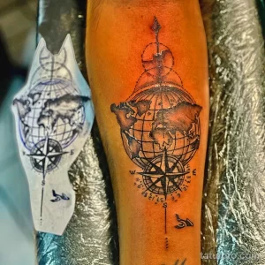 Фото татуировки Земли, заключенной в компас, выполненной в стиле blackwork с использованием плотного затенения и геометрических элементов.