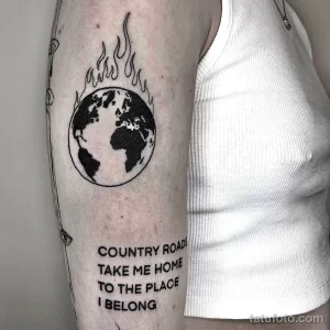 Татуировка Земли, охваченной пламенем, с надписью "Country Roads Take Me Home". Черно-белый рисунок на предплечье, символизирующий тоску по дому.