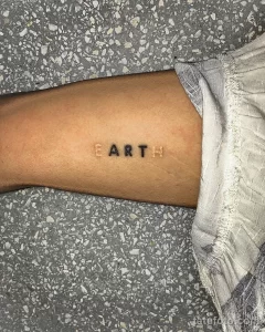 Фото тату на запястье: надпись 'EARTH' (Земля) выполненная тонкими линиями в минималистичном стиле. Небольшой и лаконичный эскиз тату.