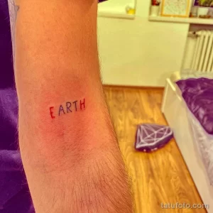 Фото тату: надпись "EARTH" на руке. Минималистичный рисунок татуировки, символизирующий любовь к планете.