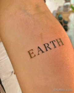 Фото тату надпись 'EARTH' на руке. Минималистичный рисунок татуировки, выполненный простым шрифтом в коричневых тонах.