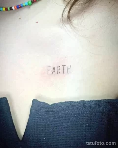 Фото простой татуировки надписью 'EARTH' на груди. Рисунок выполнен тонкими черными линиями.