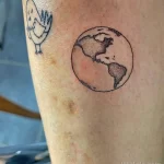 Фотография татуировки на руке с изображением Земного шара и маленького цыпленка. Рисунок выполнен в минималистичном стиле, с использованием простых линий и нежных цветов.