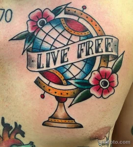 Фото тату на груди: изображение глобуса, цветов и ленты с надписью "Live Free", выполненное в стиле олд скул.