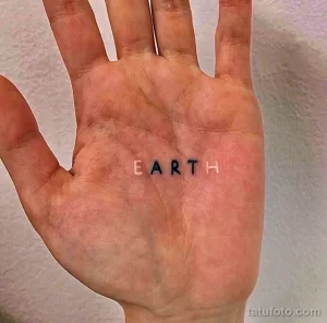 Фото тату: простая татуировка надписью 'EARTH' черным цветом, выполненная на ладони в минималистичном стиле.
