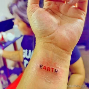 Минималистичная татуировка на руке с надписью "EARTH", выполненная простым шрифтом. Подчеркивает любовь к планете и экологическое сознание.