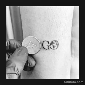 Фото тату на запястье с надписью 'GO' и изображением земного шара. Минималистичный стиль, черно-белое исполнение. Символ движения и путешествий.