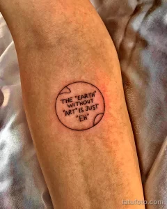 Фото тату с изображением Земли в черном контуре и философской фразой "THE "EARTH" WITHOUT "ART" IS JUST "EH"" внутри. Татуировка выполнена в минималистичном стиле.