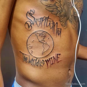 Фото татуировки на боку с изображением земного шара, ангела и надписи "The world is mine". Выполнена в минималистичном стиле с использованием тонких линий.