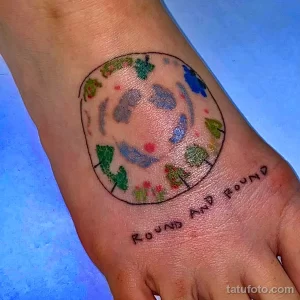 Фото яркой татуировки Земли на стопе с надписью "Round and Round". Изображение выполнено в акварельном стиле.