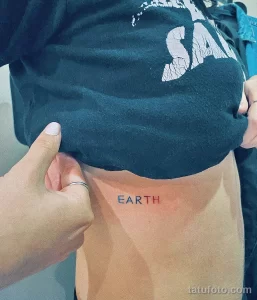 Фотография минималистичной татуировки на животе с надписью "EARTH" выполненной простым шрифтом. Черно-белый рисунок.