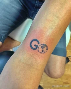 Небольшая татуировка на руке с изображением буквы 'G' и стилизованного глобуса. Черно-белый рисунок, минимализм, идея для путешественников.