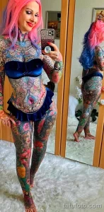 Фото тату девушки с ярким и красочным полным боди-артом и розовыми волосами. Видны детализированные изображения цветов и абстрактных узоров.