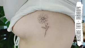 Фото тату на боку: изображение ромашки с тонкими линиями и листьями, выполненное в минималистичном стиле.