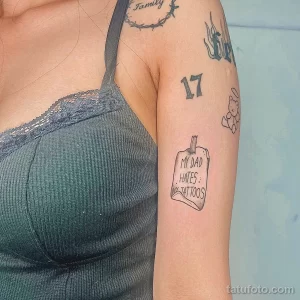 Фото тату с надписью 'My Dad Hates Tattoos' в виде свитка на руке. Черно-белый рисунок татуировки, юмористический эскиз тату.
