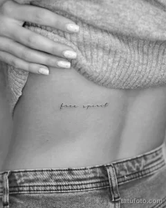 Фото тату с надписью "free spirit", выполненной тонким шрифтом на ребрах. Нежный и символичный рисунок для тех, кто ценит свободу.