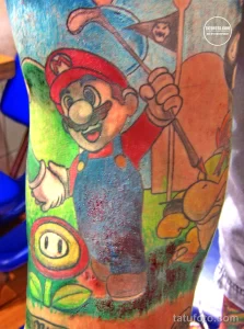 Фото тату на руке: красочный рисунок персонажей видеоигры Super Mario – Марио, Йоши и гриб, выполненный в мультяшном стиле.