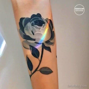 Фото тату черной розы на руке с эффектом переливов и радужных бликов, выполненной в реалистичном стиле.