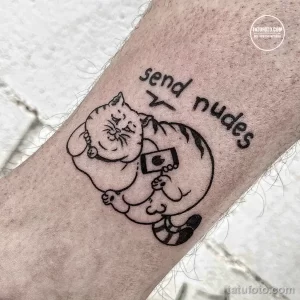Черно-белое фото тату кота, держащего телефон, с надписью 'send nudes' на руке. Минималистичный рисунок татуировки.