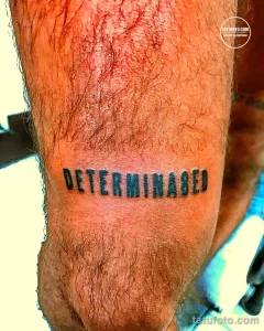 Фото татуировки с надписью 'DETERMINED' (решительный) на руке. Простой, но мощный рисунок татуировки, выполненный черными чернилами.