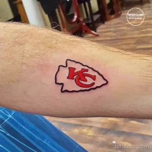 Фото тату с логотипом команды Kansas City Chiefs на руке. Простой и лаконичный рисунок в красных и белых тонах, выполненный в минималистичном стиле.