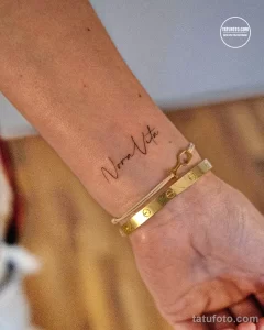 Фото тату: изящная надпись "Nora Vita" (Новая Жизнь) на запястье, выполненная каллиграфическим шрифтом. Минималистичный и стильный эскиз.