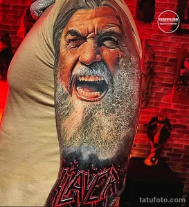 Фото тату: реалистичное изображение кричащего лица с логотипом группы Slayer на руке. Черно-белая татуировка с высокой детализацией.