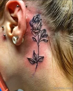 Фото тату за ухом: небольшая, изящная татуировка розы, выполненная в черно-белых тонах. Минималистичный рисунок татуировки.