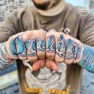 Фото тату: татуировка надписи 'Quality' на костяшках пальцев мужчины, выполненная в синих и белых тонах.