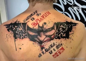 Фото тату на спине с изображением Джокера из фильма 'Темный рыцарь'. Яркие цвета, брызги краски и цитаты из фильма.