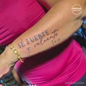Фото тату с надписью 'Sé fuerte y valiente' на предплечье. Черные чернила, каллиграфический стиль, религиозный смысл.