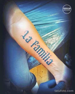 Фото тату: надпись 'La Familia' выполненная в стиле леттеринг на руке. Черные контуры, элегантный шрифт, динамичный дизайн.
