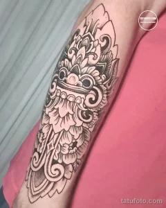 Фото тату балийской маски в стиле blackwork на руке. Детализированный рисунок с орнаментами и узорами, выполненный опытным мастером тату.
