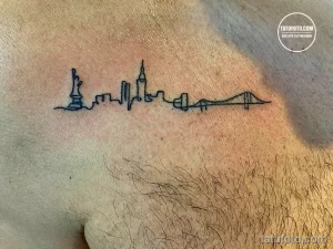 Фото тату на груди: минималистичный рисунок, изображающий силуэт города в виде кардиограммы. Тонкая линия татуировки.