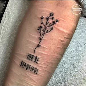 Фото тату надписи 'You're Beautiful' и ветки с цветами на руке. Минималистичный рисунок, символизирующий любовь к себе и принятие.
