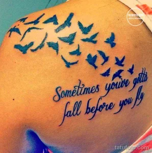 Фото татуировки на спине с изображением стаи летящих птиц и надписи 'Sometimes you gotta fall before you fly'. Рисунок татуировки в голубых тонах.