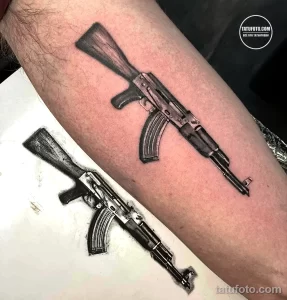 Фото тату: реалистичная татуировка двух автоматов Калашникова, расположенная на ноге. Детализированный рисунок татуировки в черно-серых тонах.